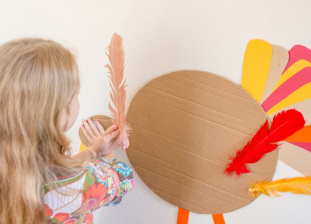 A girl holds a feather as she plays the Thanksgiving game Pin the Feather on the Turkey