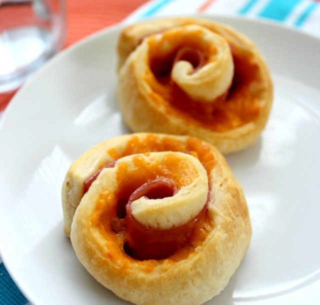 Two ham and cheese roll ups sit on a plate ready to eat by even the most picky of eaters