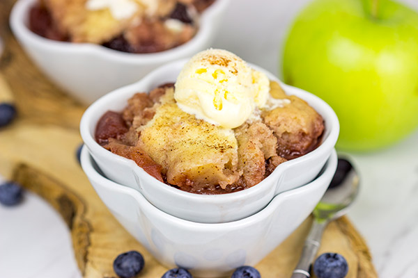 Two small bowls of blueberry apple cobbler topped with whipped cream