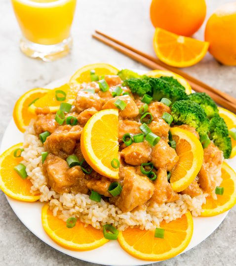 A plate of slow cooker orange chicken garnished with sliced oranges