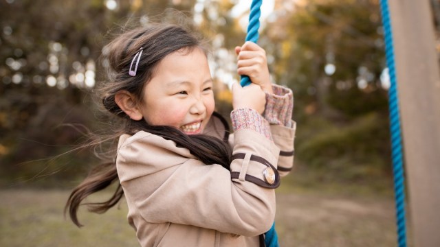 a girl swing from a tree swing during fall with leaves falling around