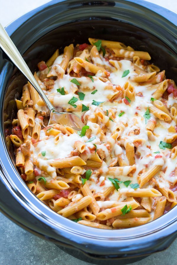 A pot of slow cooker baked ziti with a serving spoon