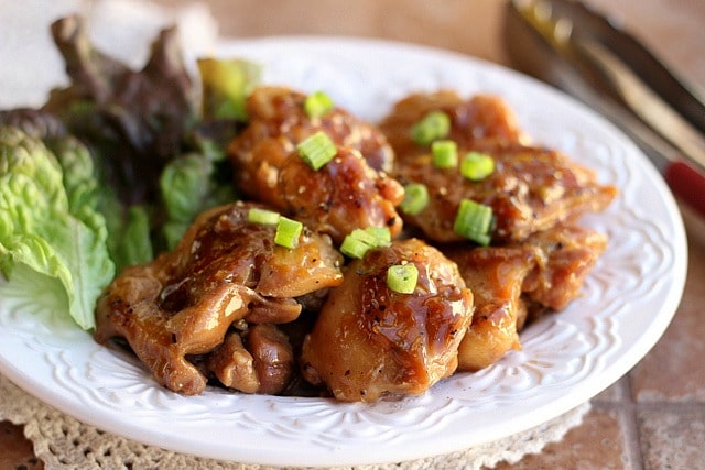 Apple Juice Chicken topped with green onions sits on a white plate garnished with lettuce