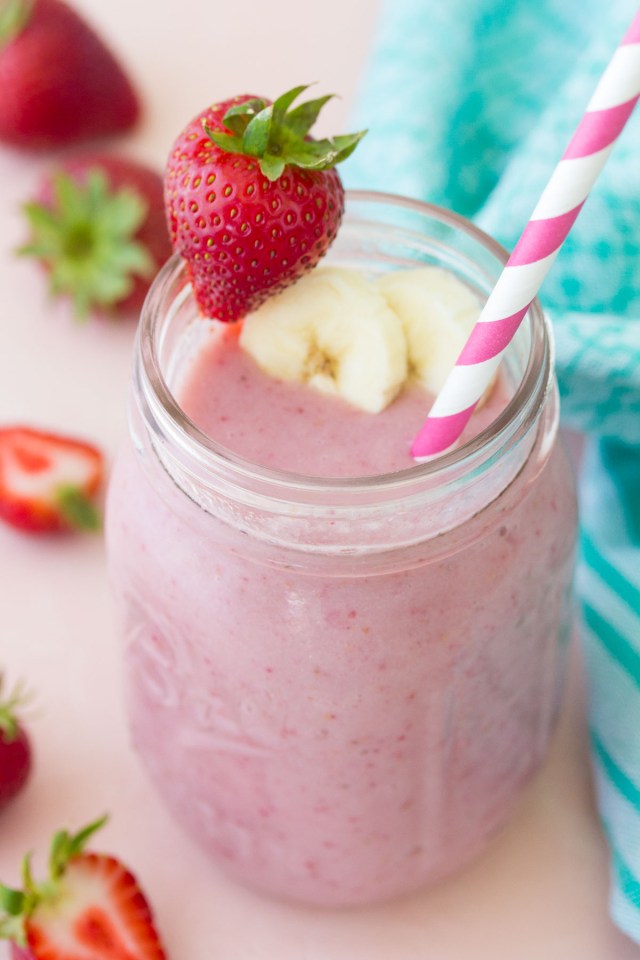 A pink smoothie that secretly contains healthy veggies is in a jar topped with a strawberry and banana
