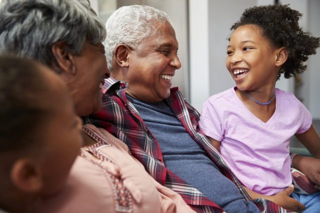 Happy grandparents spending time with their grandchildren sit on a couch laughing