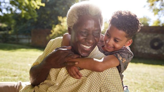 a boy hugs his grandpa from behind on a sunny day