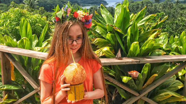 girl with flower headband drinks tropical drink from coconut