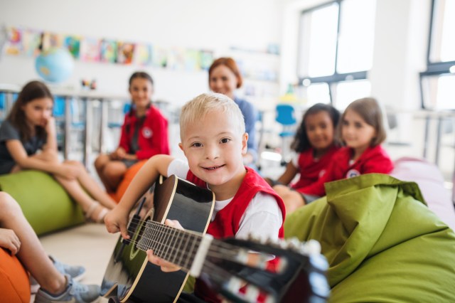 A boy plays guitar as he's watched by other children