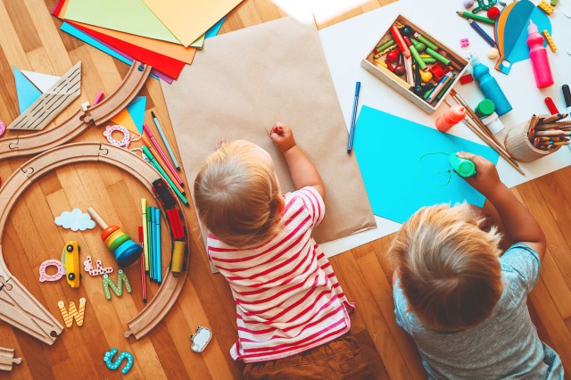 A toddler stretches out on the floor to draw using school supplies