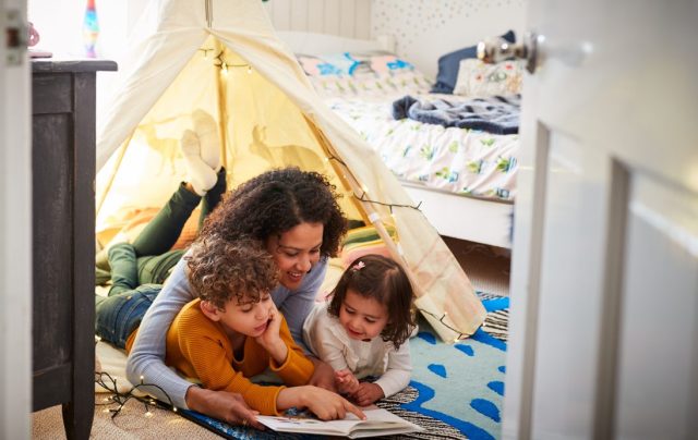 A mom and two children read in a fort that they made on the floor