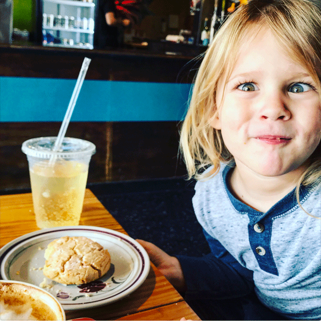 A child makes a silly face at the camera while sitting at a table eating and drink at the Bookclub Cafe