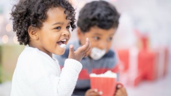 two kids sit drinking hot cholocate seattle with in red cups with whip cream