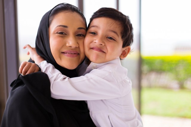 A young boy wraps his arms around his smiling mother in affection