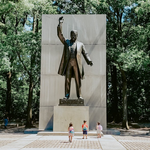 three children looking up at a statue of Theodore Roosevelt