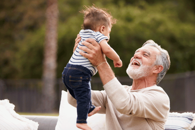 A grandfather happily lifts his baby grandson into the air