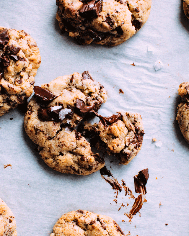 A gooey chocolate cookie broken into pieces next to other chocolate chip cookies