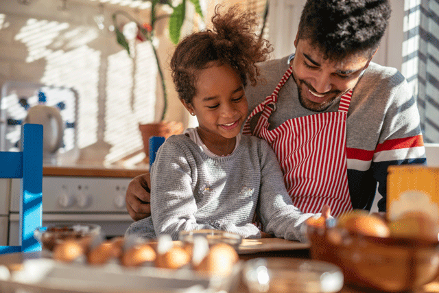 A father and daughter stand over eggs in the kitchen baking together
