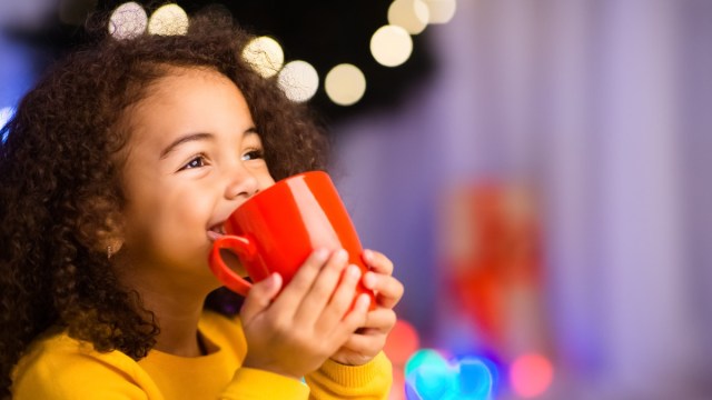 a girl sips hot chocolate portland in a red cup with a lit tree behind her