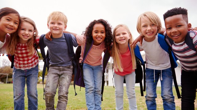a group of kids wearing backpacks on a warm day looking happy for mid-winter break camps