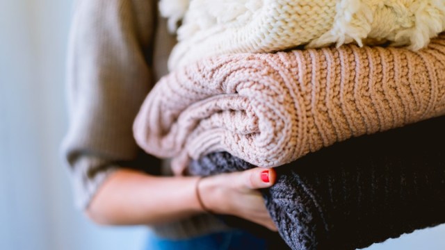 a woman holds a stack of kids clothes to donate