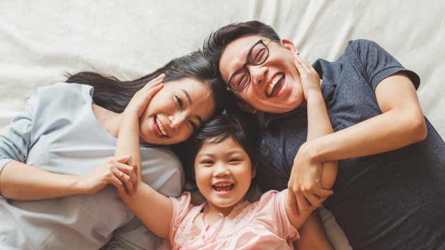 a family of three laughs on the bed
