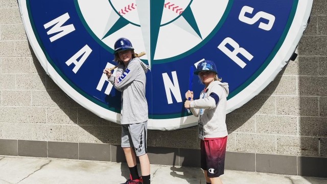 Boys pretend to swing bats in front of the Mariner's logo at T-Mobile park