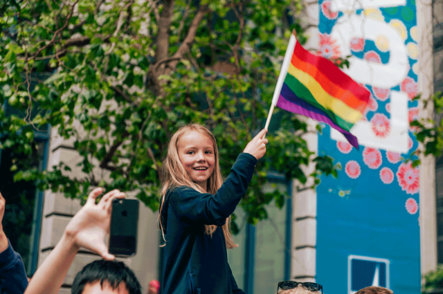 girl holding rainbow pride flag in parade