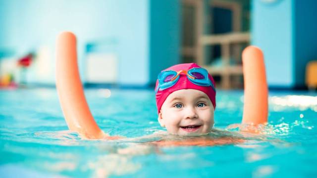a girl swims with a pool noodle at an indoor swimming pool