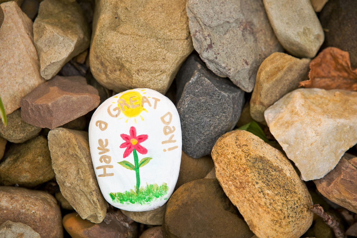 painted rock saying have a great day with a flower
