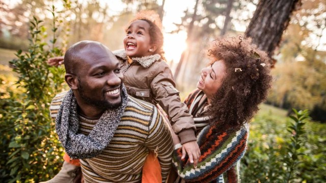 a family of three hikes through a sunny forest in fall