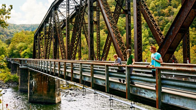 Bridge over a river and three onlookers standing on the bridge .