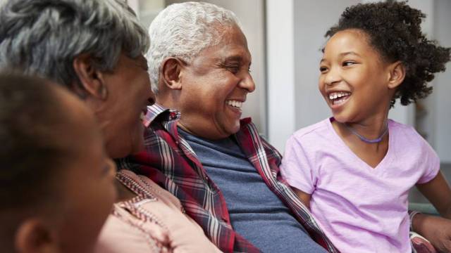 A little kid smiles at grandparents on a couch on Grandparents Day