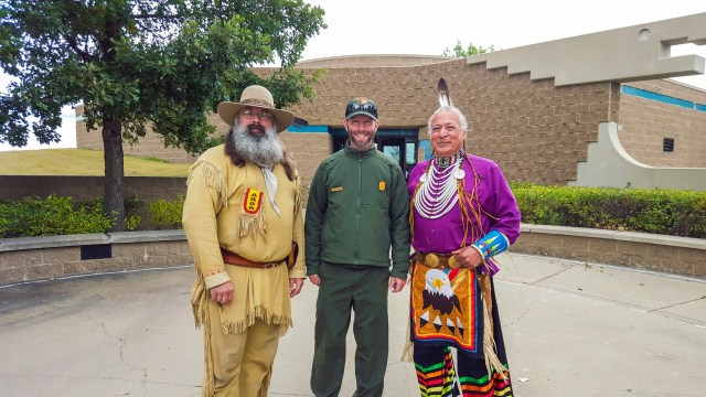 Two mein Native American attire standing on either side of a park ranger.