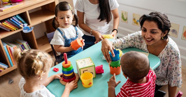 Children sit around a table with their teachers at daycare.