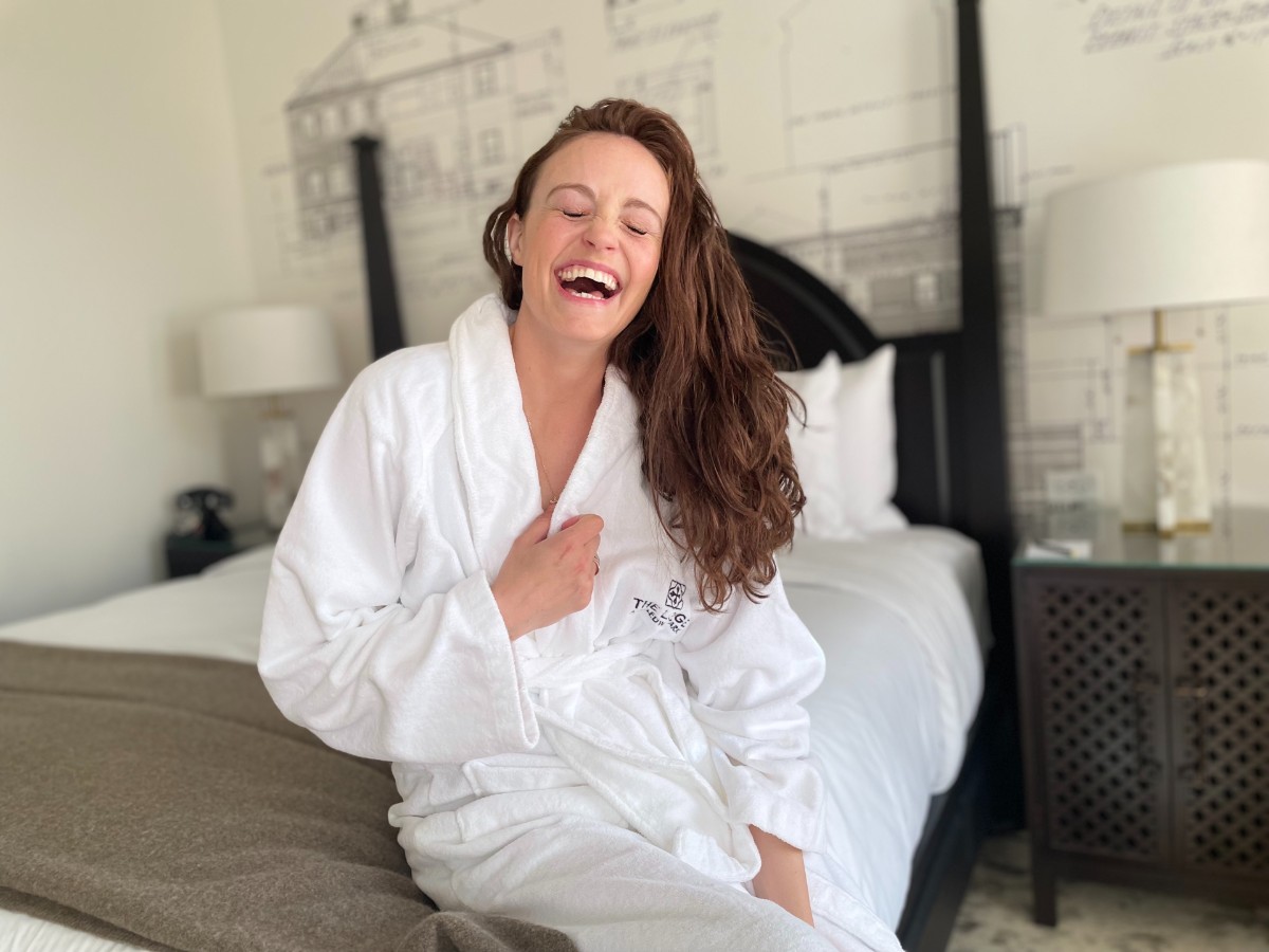 a mom laughs on a bed in a bathrobe at the lodge at st edwards a girls weekend trip from seattle destination