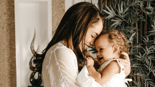 a mother snuggling her baby with pierced ears for a story on what to know about infant ear piercing