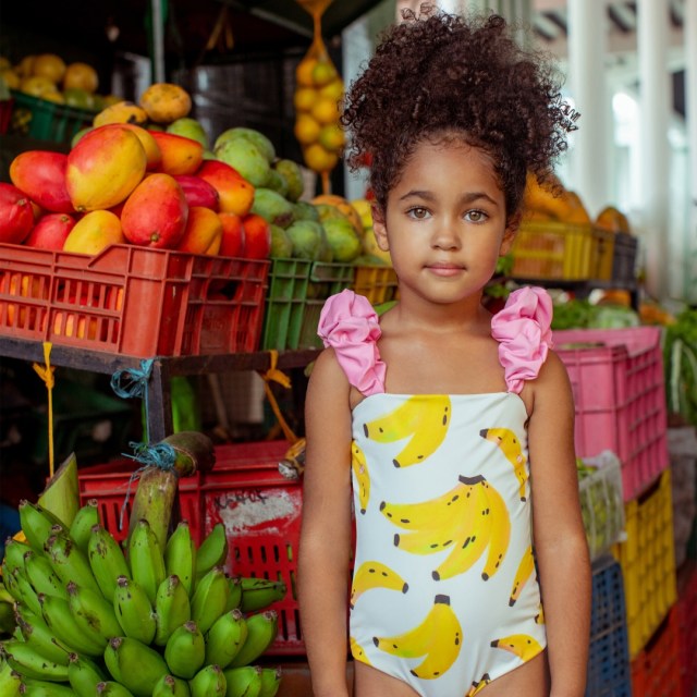 child wearing the bathing suit in front of a fruit display