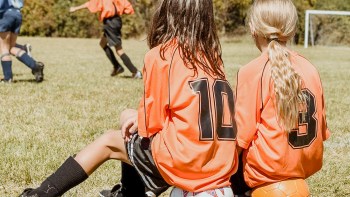 two girls watching soccer game from the sidelines