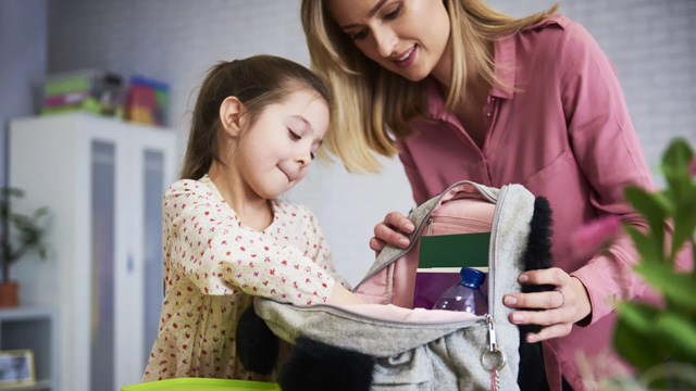little girl packing her backpack, an easy morning chore for kids