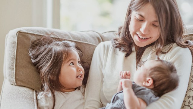 a mom holding a newborn while her toddler looks on for a story on what not to say to a toddler after a new baby