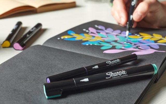 a person using Sharpie markers on black paper