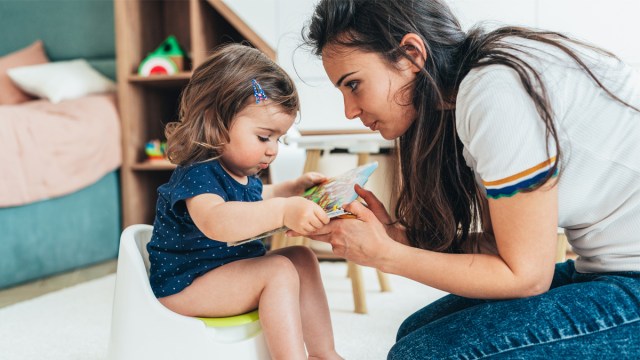 a little girl sitting on the potty beside her mom, who now knows when to start potty training and common mistakes to avoid