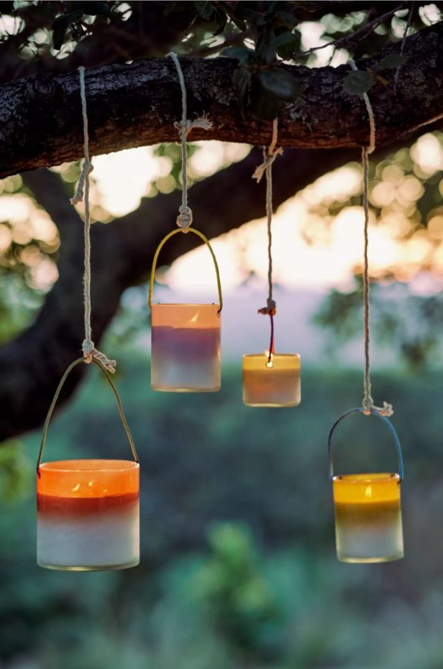four colorful hanging citronella candle lanterns hanging from tree branches at dusk