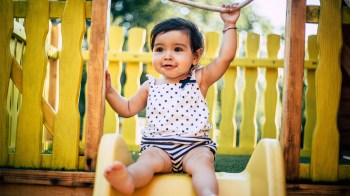 a baby on the slide after her mom checked that it's not too hot from the sun, one of our summer safety tips