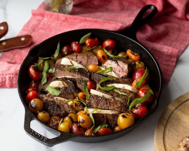 cast iron skillet on table filled with a roasted steak dish