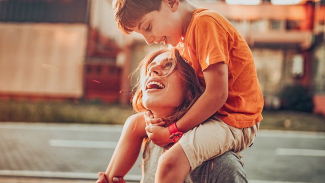 beautiful mom with healthy skin holding son on her shoulders