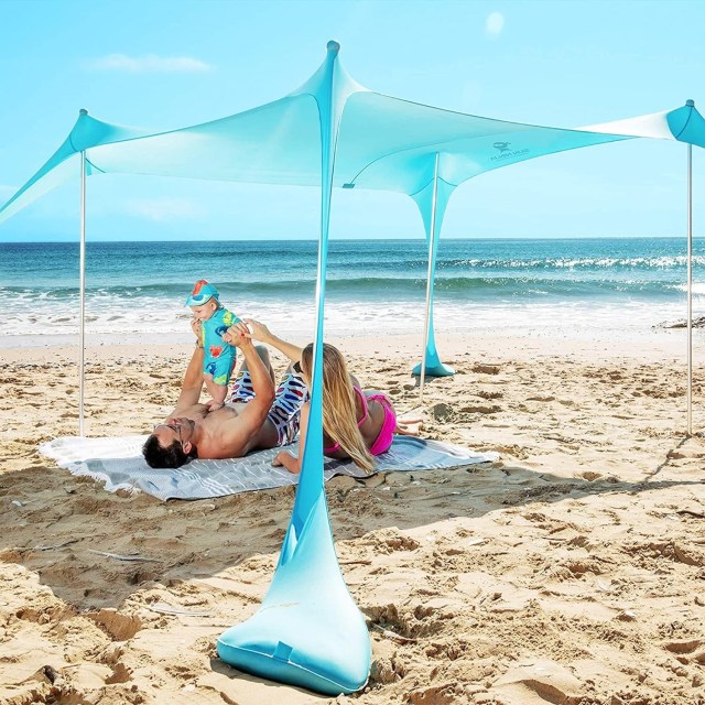family laying on beach under sun tent