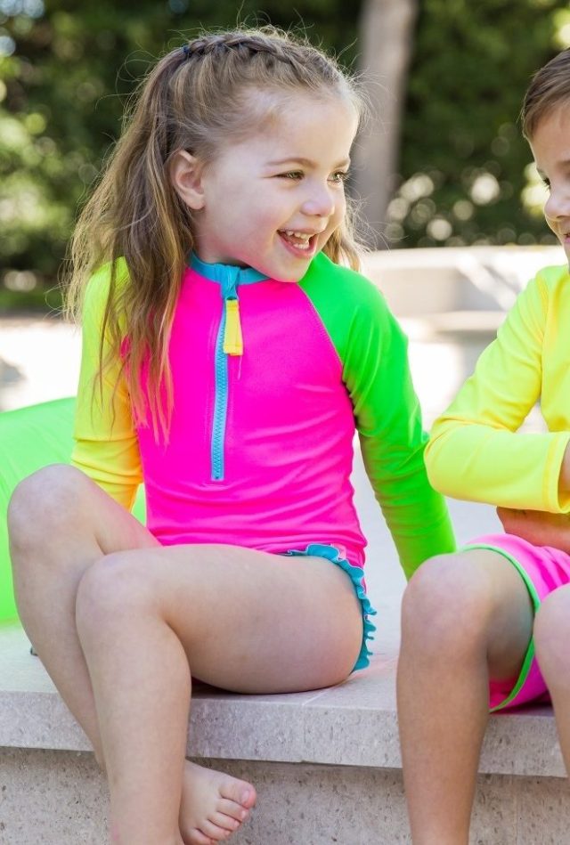 child in neon swimsuit sitting poolside
