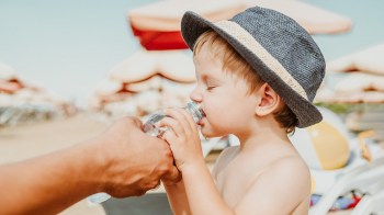 a little boy drinking some water on the beach alongside some hydrating foods like cantaloupe