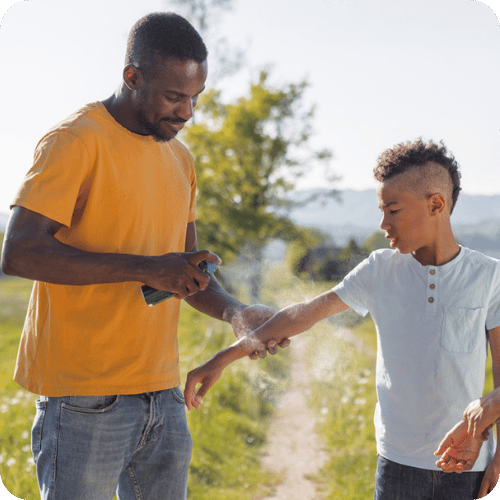 a dad spraying bug spray on his son to prevent mosquito bites